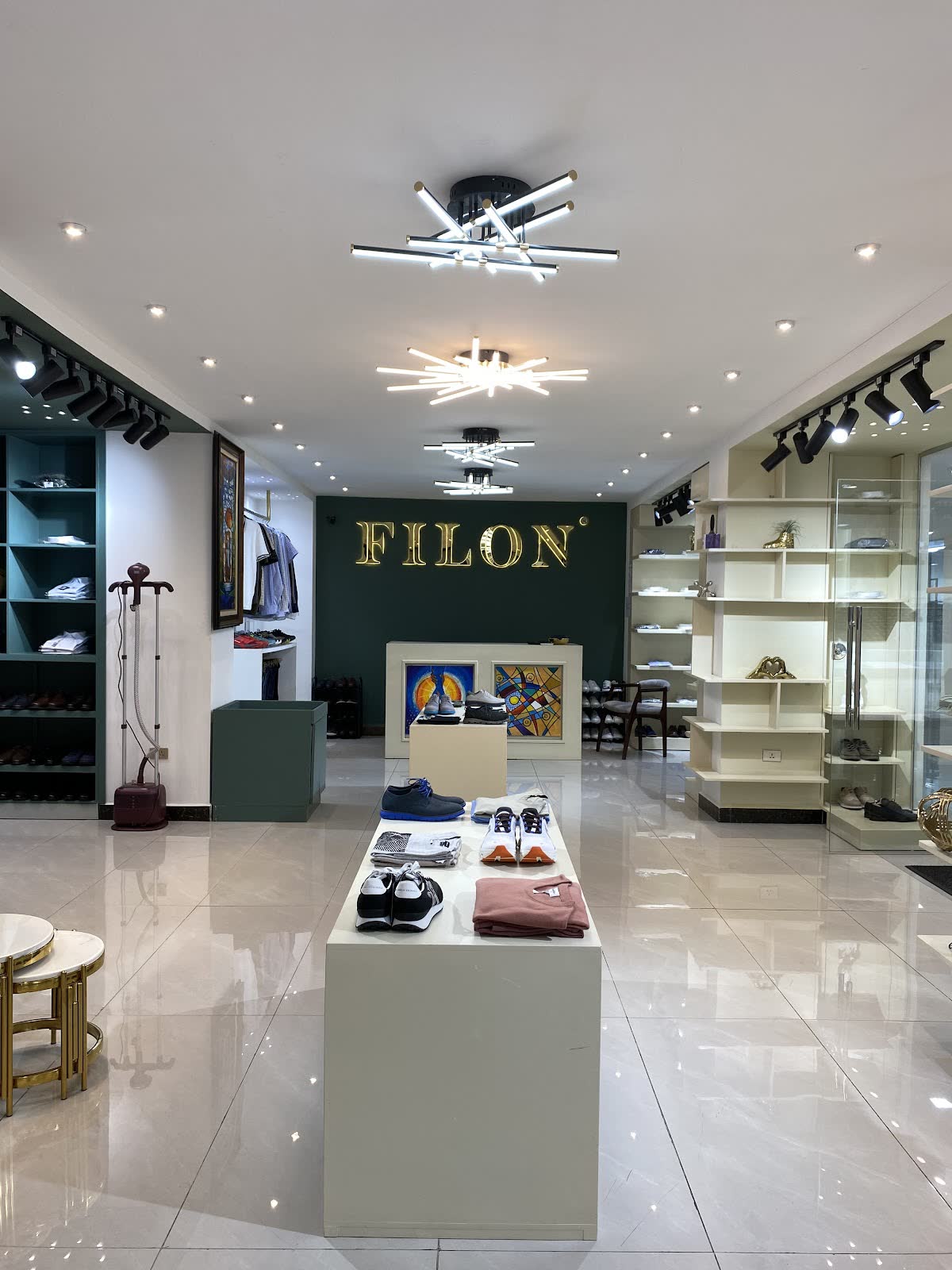Inside a FILON showroom: gold FILON sign on a green wall, a display table of shoes and knitwear, and white shelving